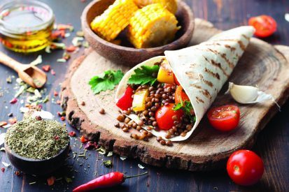 Vegan tortilla wrap, roll with grilled vegetabes and lentil and boiled corn cob on a wooden background